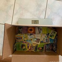 Cardboard box of Pokémon cards sitting on scale reading 8.5 lb