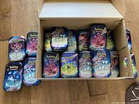 Shoebox open showing interior packed with Pokémon Paldean Fates mini tins plus several stacked outside
