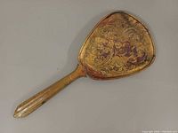 Back of brass hand mirror showing ornate floral design and patina