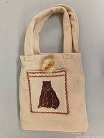 Front of beige felt tote with bear embroidery and handles