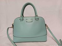 Front view of mint green Kate Spade Wellesley satchel showing logo plaque, handles, strap attachment
