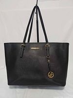 Front view of black saffiano leather tote with MK logo and charm