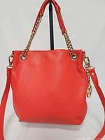 Front view showing red pebbled leather, chain handles, logo charm, shape
