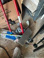 Group of cleaning tools on floor including red-handled mop, duster and patterned-handle foam cleaner