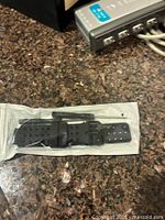 Sealed pouch containing black perforated watch strap and screwdriver