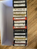Stack of 8-track tapes in a box, labels facing up showing several artist and title names