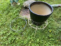 Ceramic planter on white metal stand next to black metal ring stand on grass
