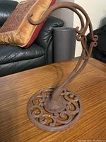 Angled view of entire wrought iron stand showing scrollwork base and curved arm