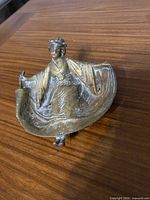 Front view of brass ashtray showing robed female figure and bowl