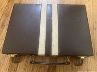 Closed brown faux-leather backgammon case with cream stripes, handle and latches visible