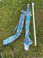 Folded beach umbrella, fabric carry sleeve, two-piece white pole on grass