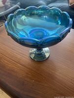 Side view of blue iridescent carnival glass pedestal bowl showing stem and scalloped rim