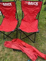 Two red The Brick folding camping chairs with carry bags on grass