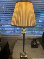 Lamp standing on table illuminated, showing metal column, ornate base, pleated shade
