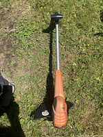 Full view of orange string trimmer laying on grass