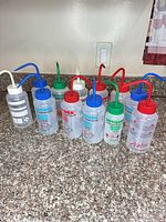Front view of eleven translucent plastic wash bottles with colored spouts