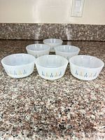 Front view of six white milk glass plates with blue and gold starburst band