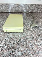 Front angled view of Apple external 800K floppy drive with attached cable