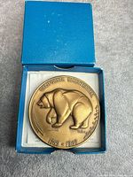 Medal in open blue box showing obverse bear design and leaflet underneath