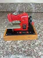 Front view of red toy sewing machine on wood base