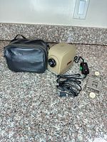 Projector, carrying case, power cord with inline switch, slide/film mount on countertop