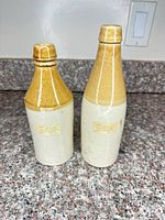 Front view of both stoneware ginger beer bottles showing two-tone glaze and overall condition
