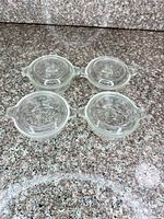 Top view of four clear glass Pyrex bowls with lids displayed on countertop