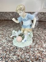 Front view of glazed porcelain figurine showing boy, dog and ball