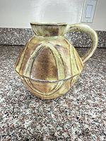 Front view of bulbous brown and green glazed stoneware pitcher with handle