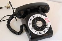 Overall view of black rotary desk phone showing rotary dial and handset