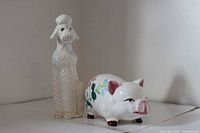 Poodle figurine beside piggy bank, full view