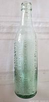 Full upright view of embossed aqua glass bottle