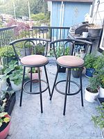 Two matching black metal bar stools with taupe seats on balcony