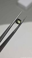 Oval green sapphire held in tweezers side profile