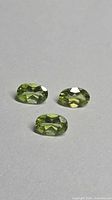 Three oval-cut apple green peridot stones on neutral background