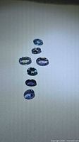 Seven oval-cut bluish-violet gemstones on white background