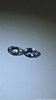 Two oval faceted blue-purple gemstones on neutral background