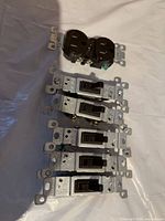 Five black toggle switches and one duplex outlet arranged on table