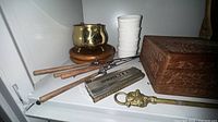 Shelf view showing jewelry box, ramekins, brass pot, skewers, harmonica, brass rod