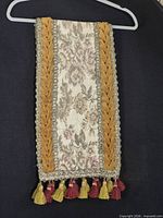 Full view of folded table runner showing floral tapestry panel, velvet borders, tassel fringe