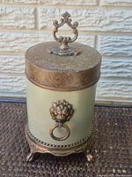 Front view of canister showing lid, finial, lion head ring handle, footed base