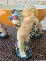 close-up of one cherub support showing floral garland and section of yellow bowl
