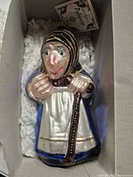 Front view of glass old woman ornament inside box
