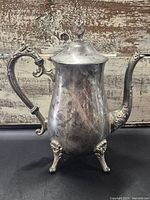 Full view of ornate silverplate coffee pot on four feet