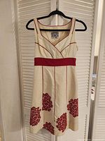 Front view of cream dress with red accents and floral hem