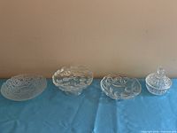 Four clear glass pieces lined left to right: bubble bowl, pedestal compote, floral bowl, lidded candy dish