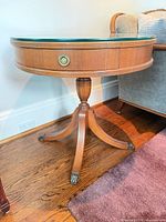 Full view of Delcraft round side table showing glass top, drawer, pedestal legs, brass feet