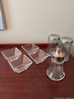 Four square glass bowls and three shakers grouped on tabletop