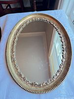 Front view of oval gold gilt mirror displaying frame details and glass