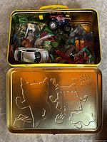 Open lunchbox displaying assorted toys including cars, airplane, bagged figures